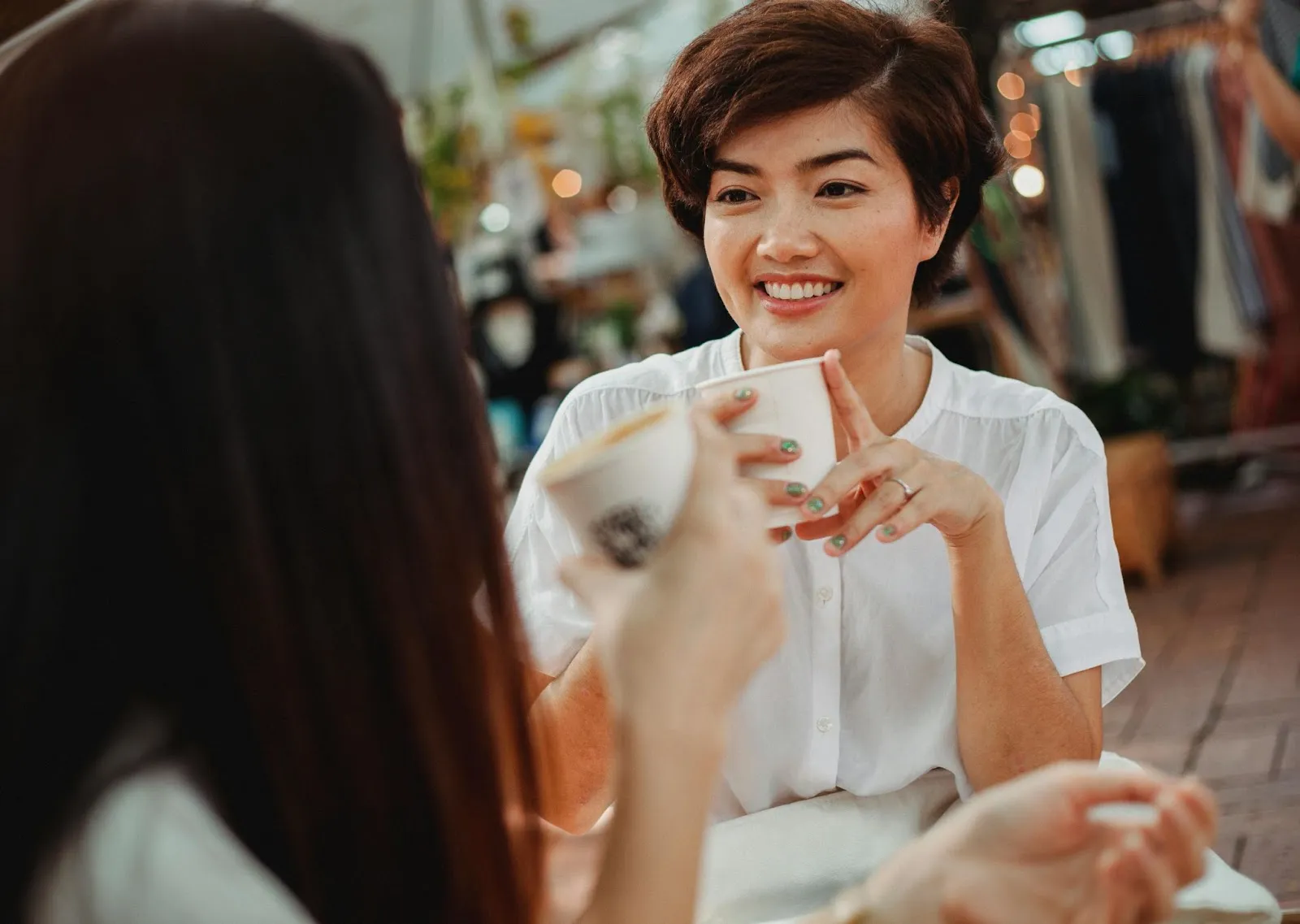 A woman smiles and chats with her friend at a coffee shop.