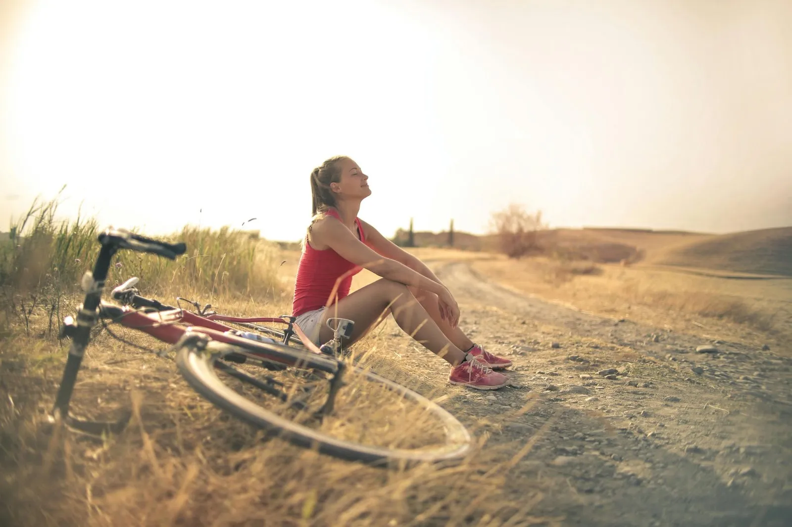 A woman relaxes by the roadside with her bike laying on the ground next to her.