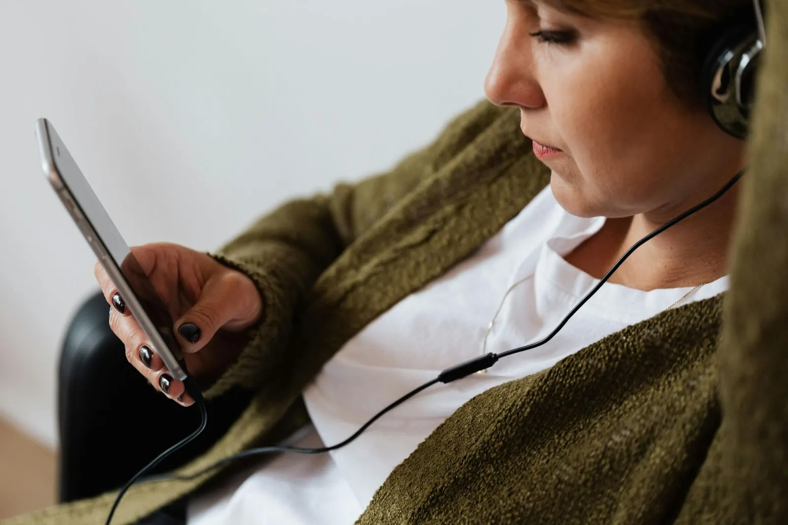 A woman listens to headphones while looking at her phone.
