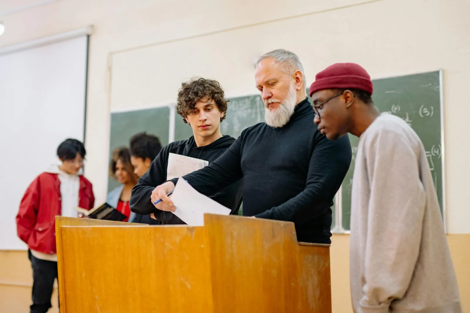 An older teacher looks at a paper with two high school students looking over his shoulders at the paper.