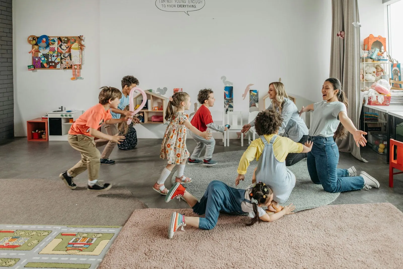Two female teachers play on the floor with a small group of primary school students.