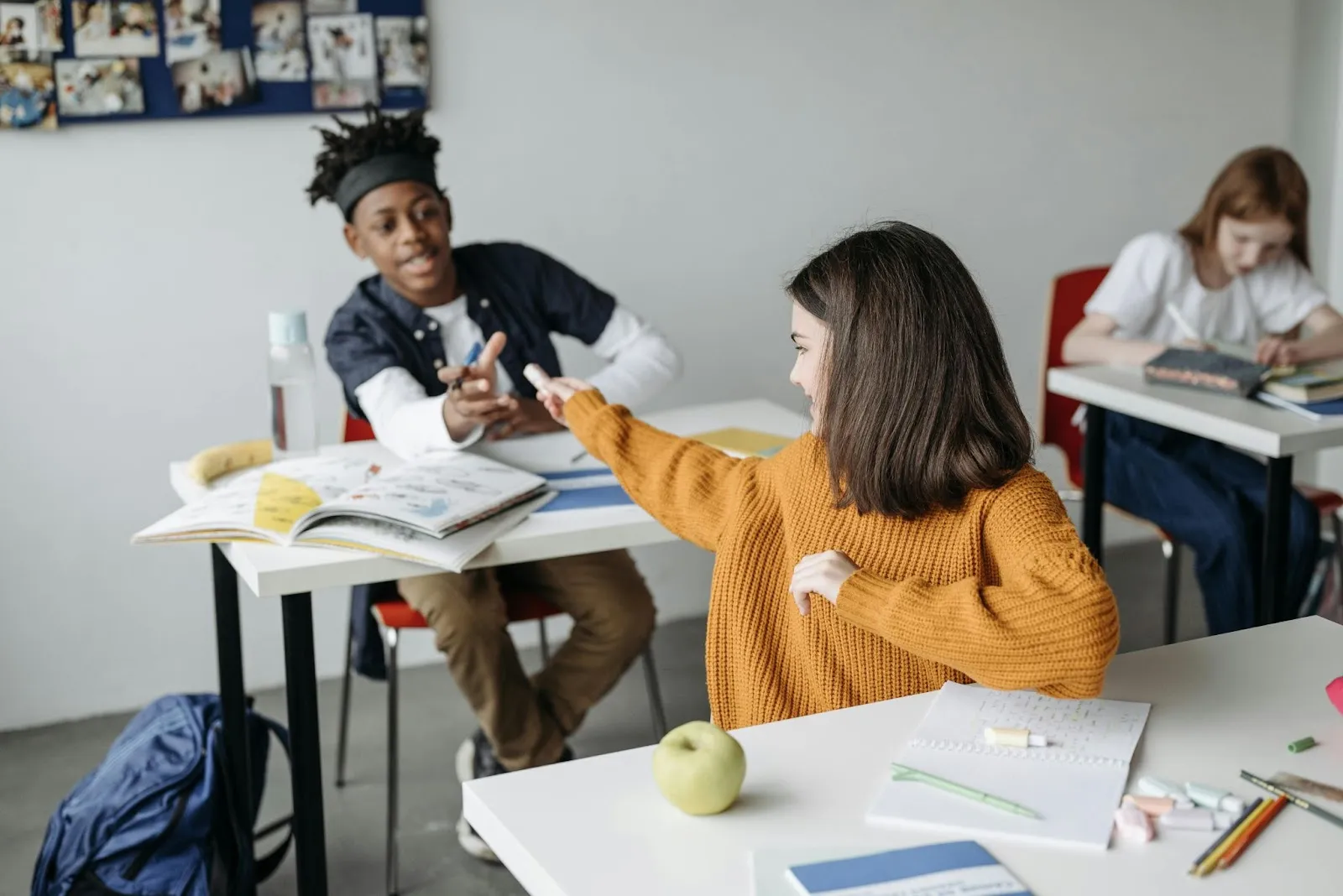 A student passes a glue stick to the person seated behind her.