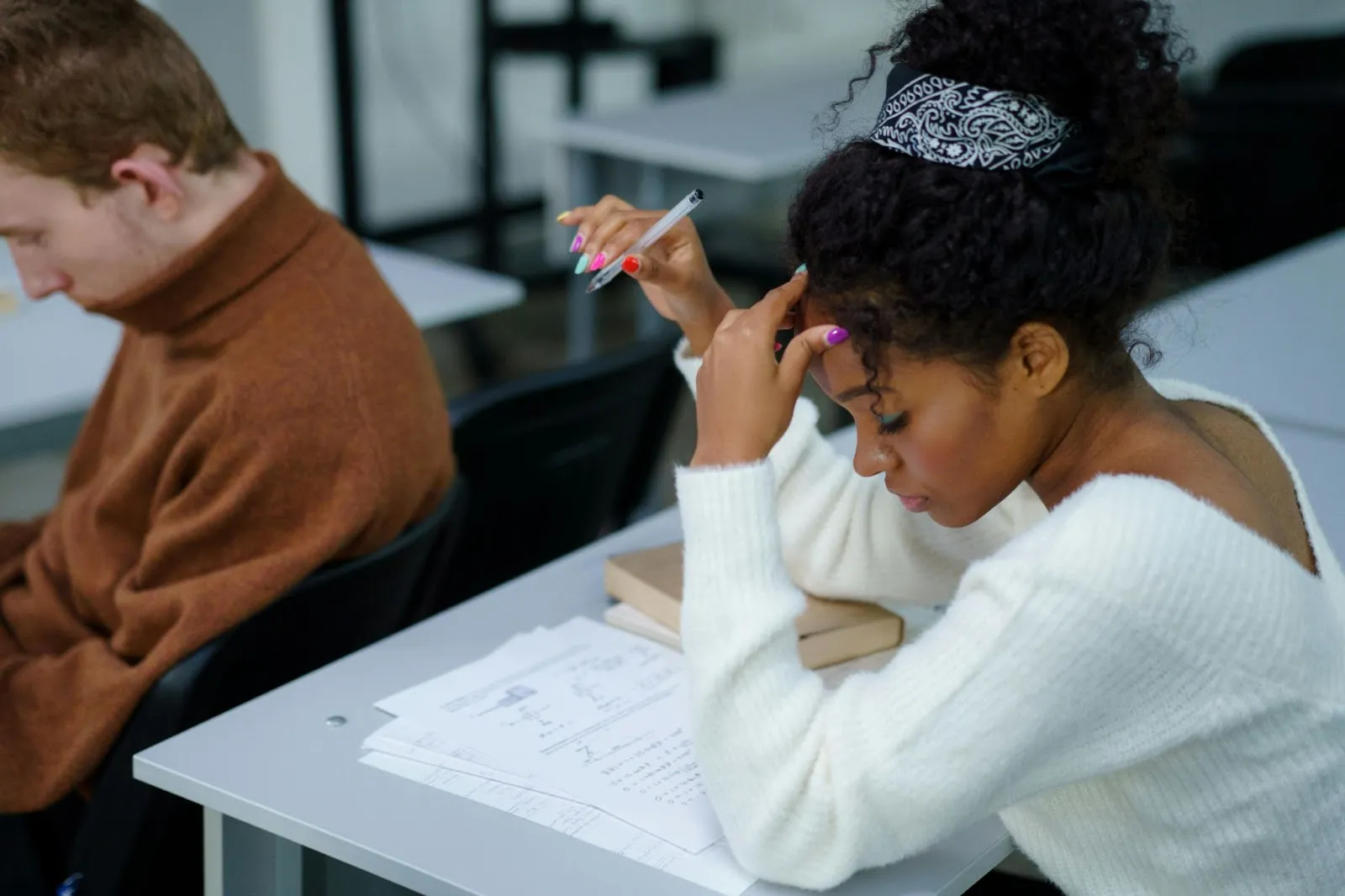 A high school student focuses on a set of pages in front of her, pen hovering in the air beside her head.