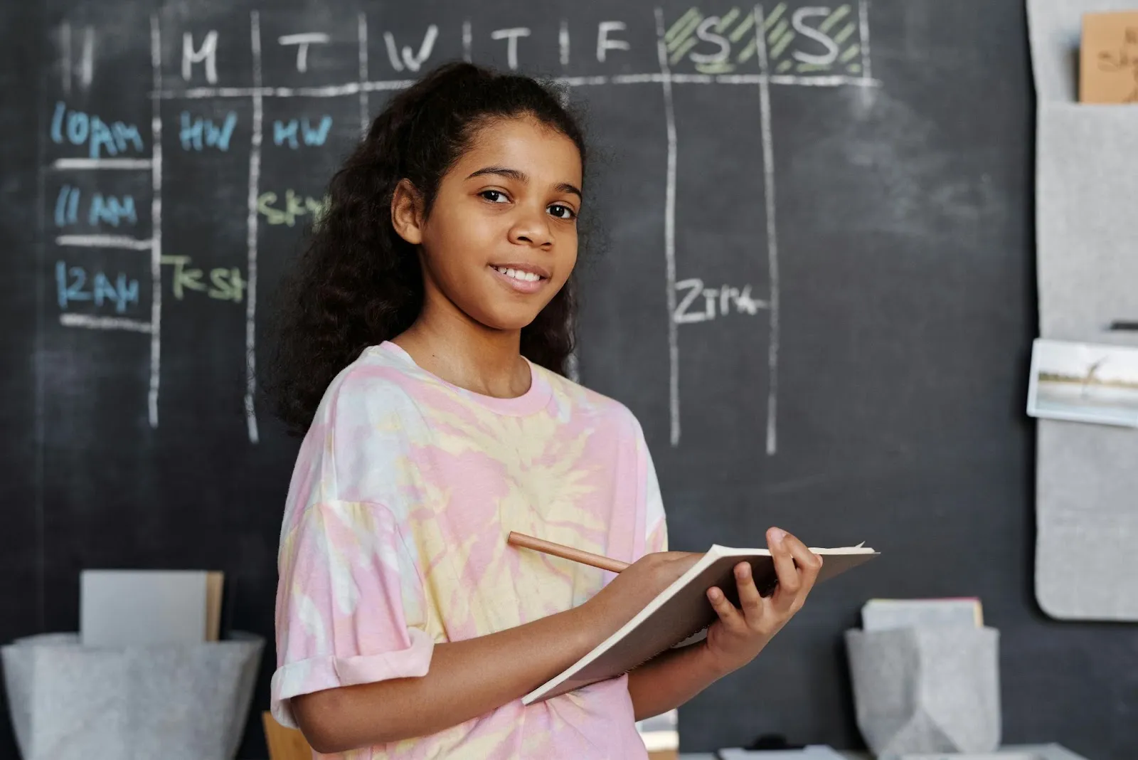 A student faces the camera confidently while she writes in her notebook.