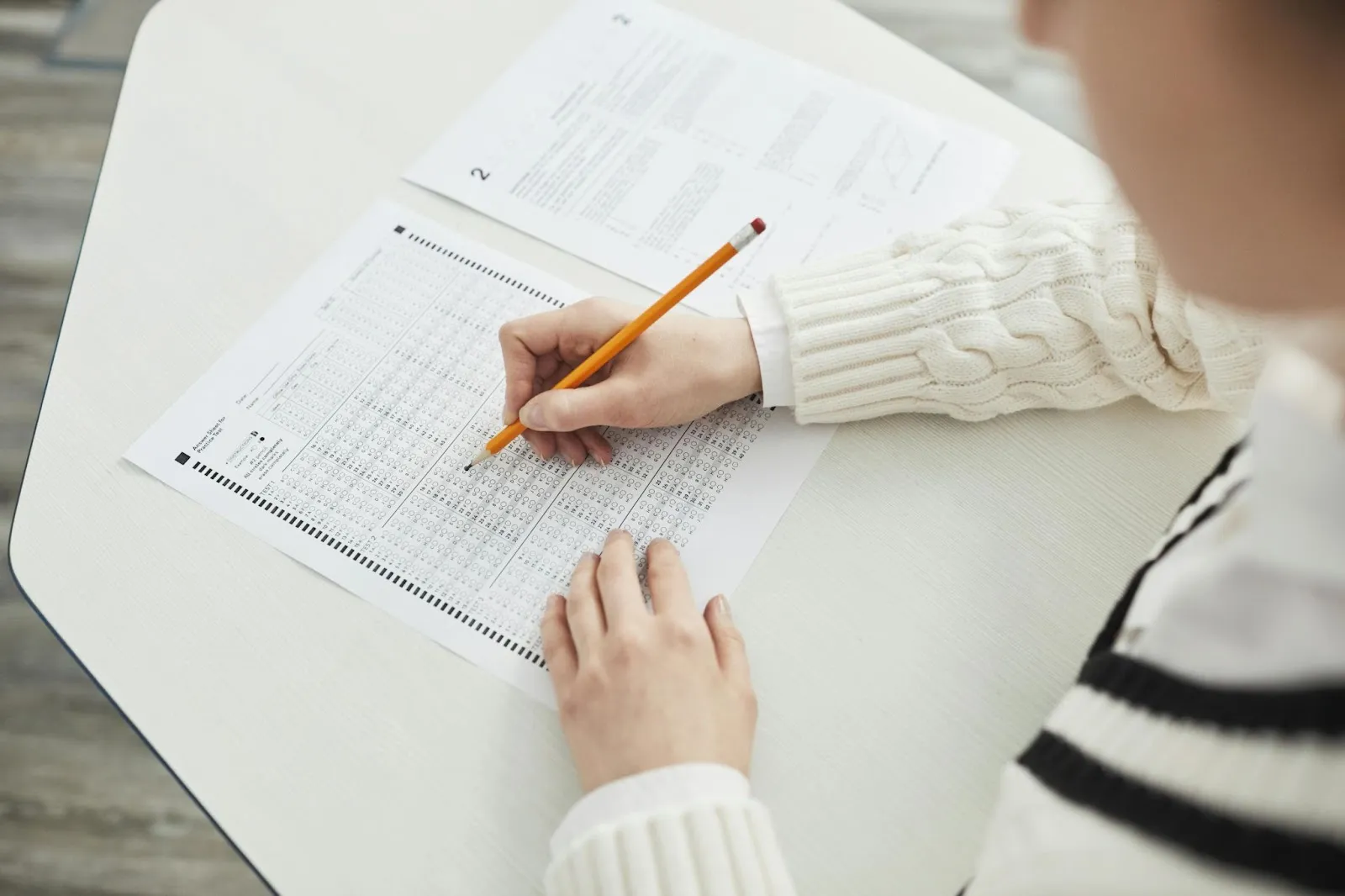 A student hovers their pencil over a bubble sheet for the exam to his right.