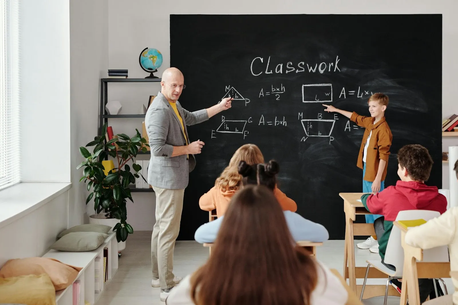 A teacher and his student assistant discuss geometry using figures on the blackboard.