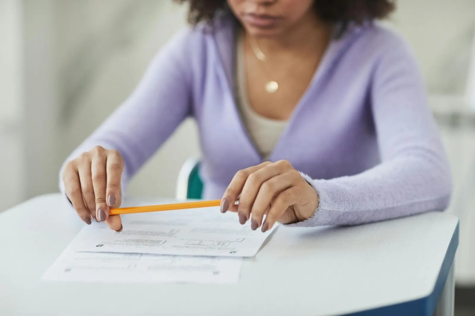 A student hovers her pencil thoughtfully over the exam as she contemplates the questions.