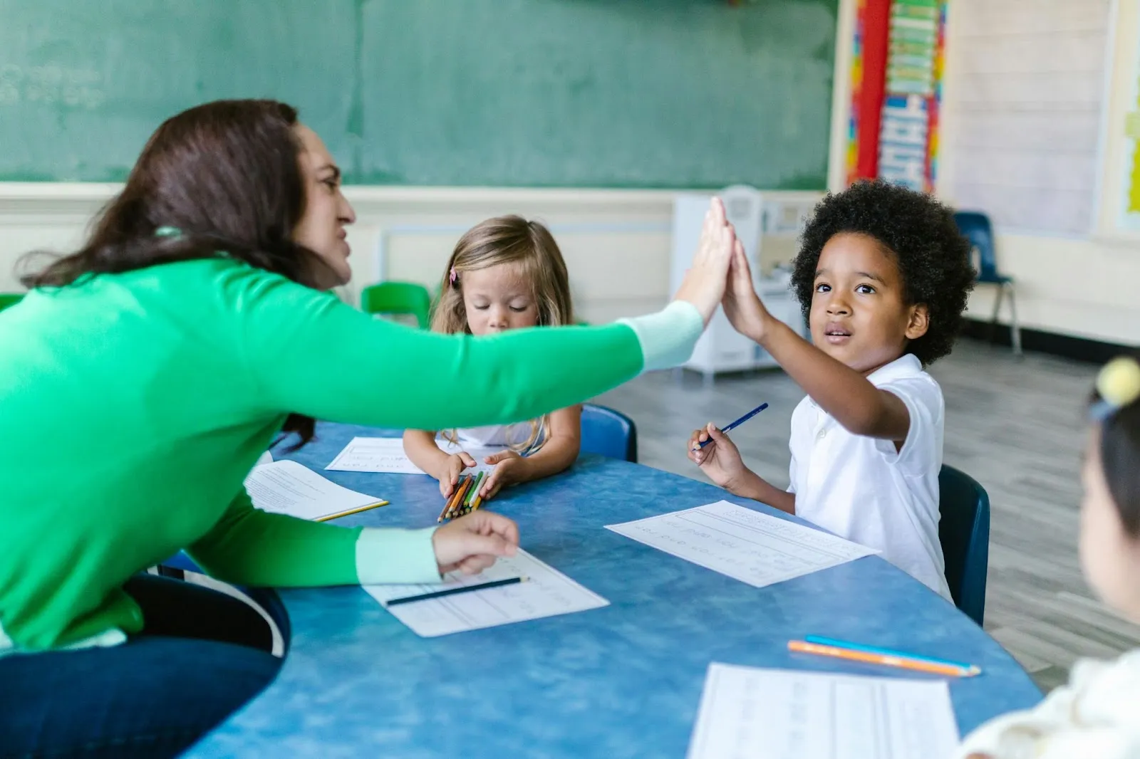A teacher high-fives her student at their small group table.