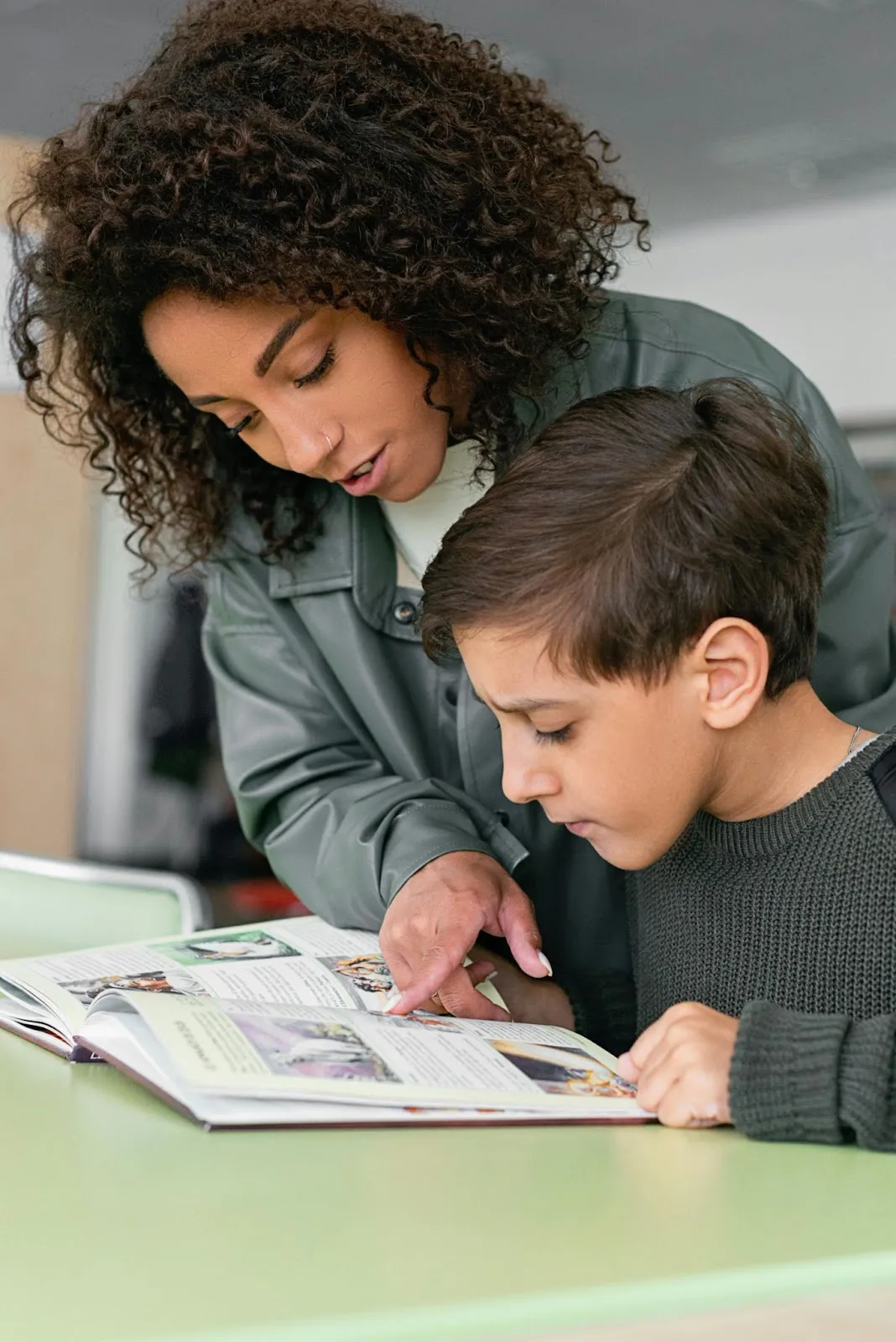 A teacher leans over her student to point out something in his reading.