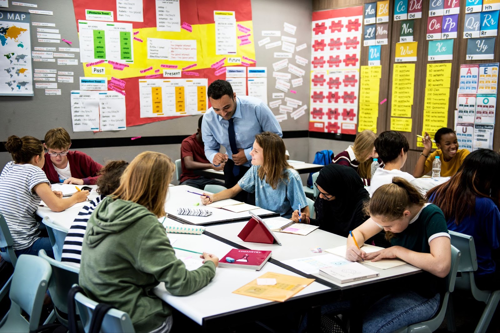 A teacher engages with a student at a full group. Decorations litter the walls.