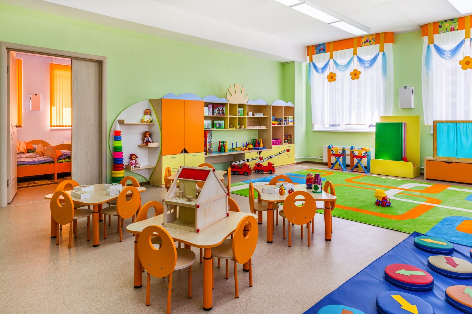 A colorful primary school classroom empty of students. The walls are green, learning toys are scattered about the room.