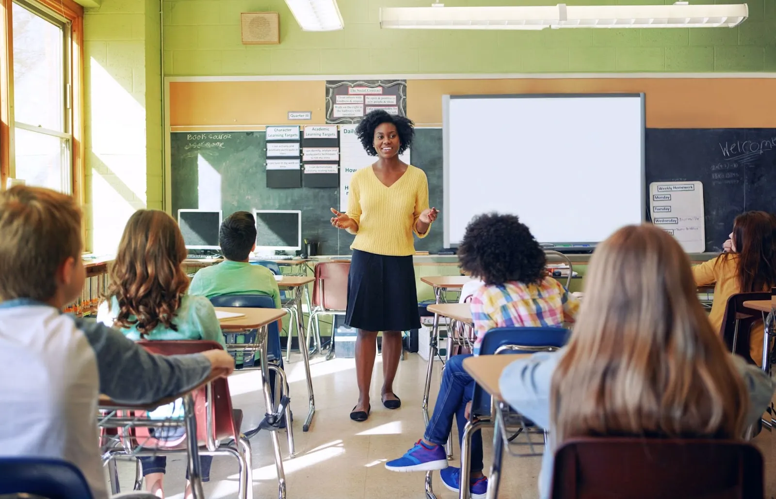 A teacher stands at the head of a full classroom of students.