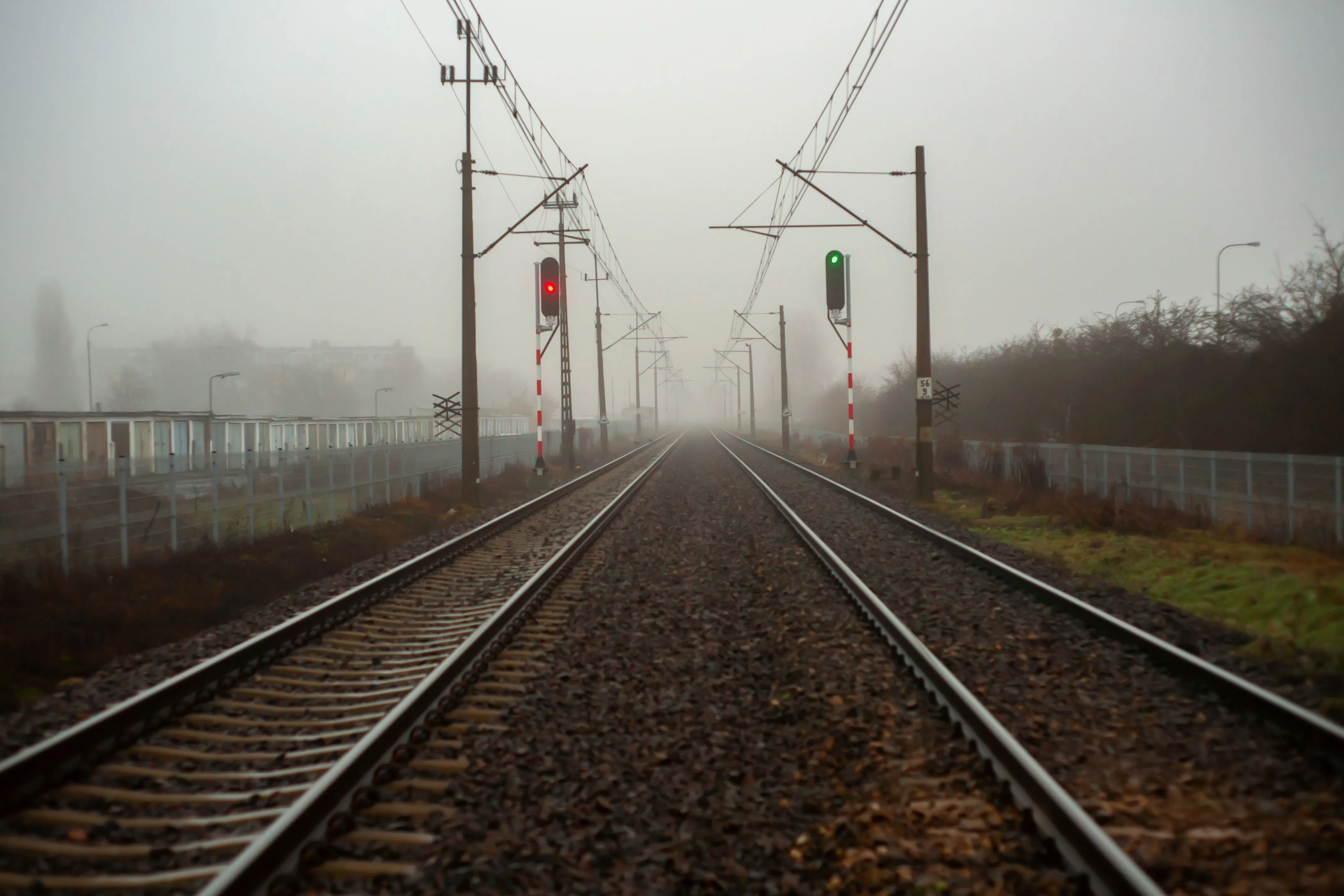 Railway tracks disappearing into fog with red and green signals, creating a moody landscape that evokes distance, reduced visibility, and unclear direction.