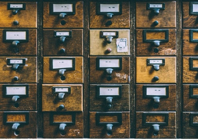 A wall of small wooden library catalogue drawers, all closed, with a handwritten note tucked into one label slot.