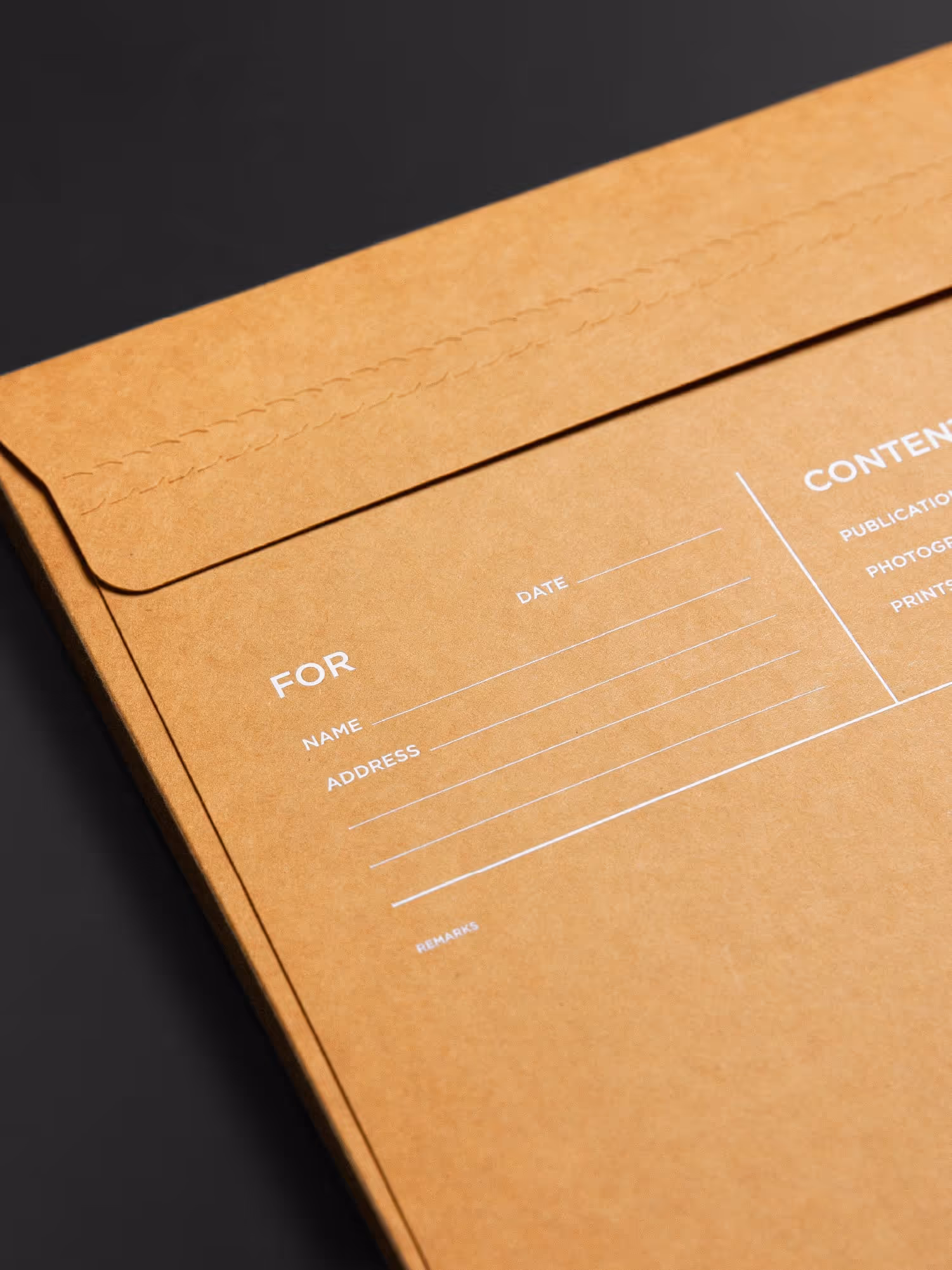Close-up of a brown paper envelope with printed white lines and text fields labeled 'FOR', 'Name', 'Address', and 'Date' on a dark surface.