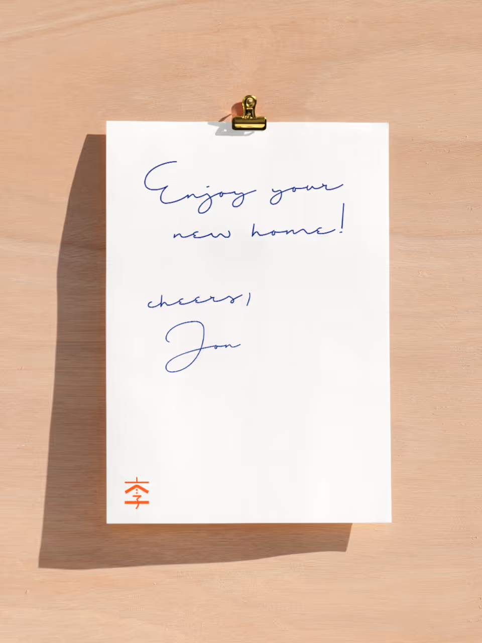 White paper clipped to a wooden board with handwritten note saying 'Enjoy your new home! cheers, Jon' and a red stamp at the bottom left.