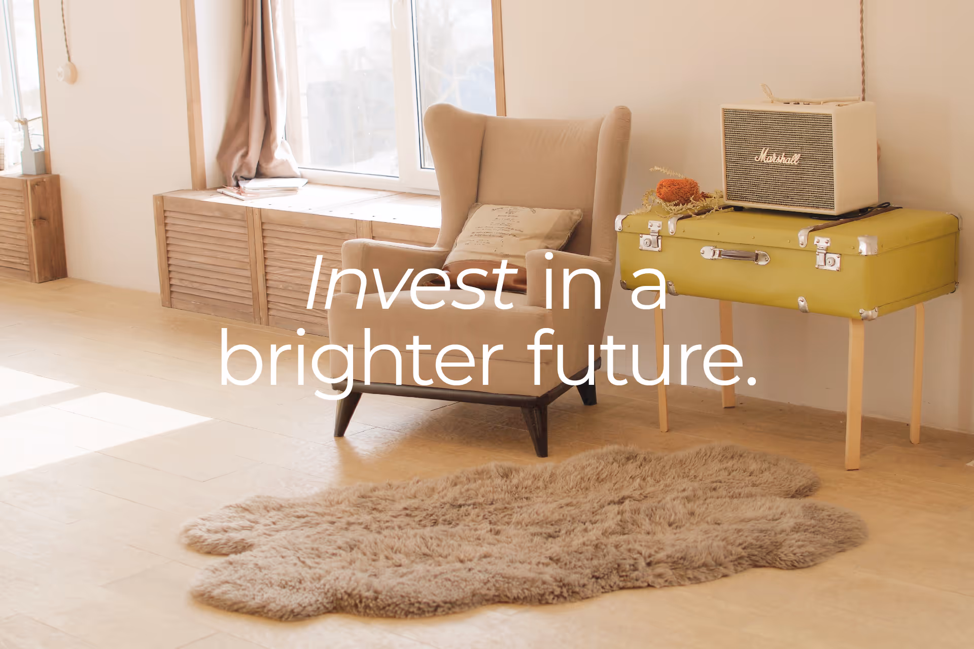 Cozy beige armchair with pillow near window, next to a vintage green suitcase table holding a Marshall speaker, with a fluffy beige rug on light wooden floor.