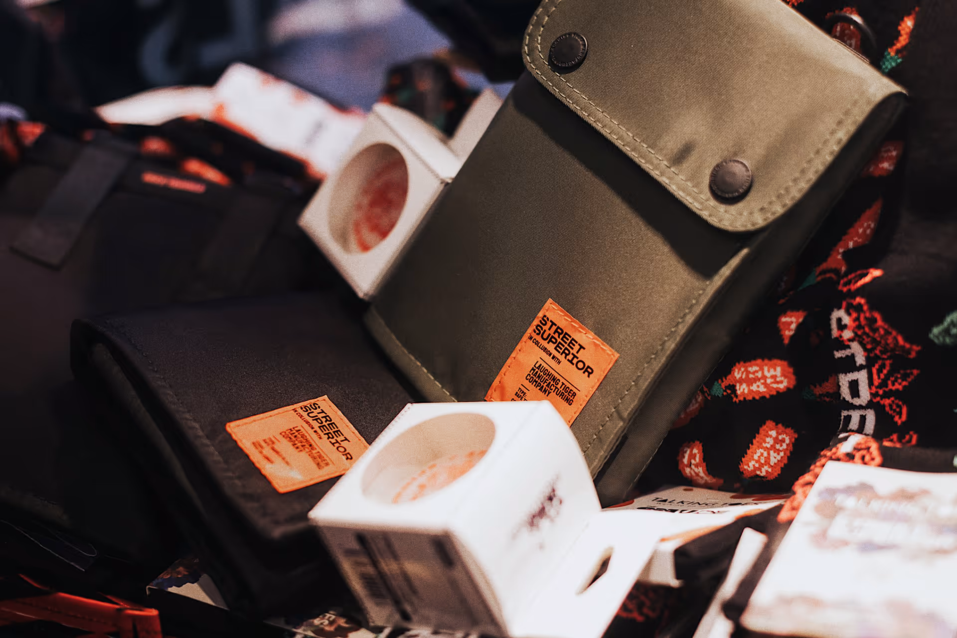 Two fabric pouches with orange 'Street Superior' labels, displayed with white boxes and a patterned cloth in the background.