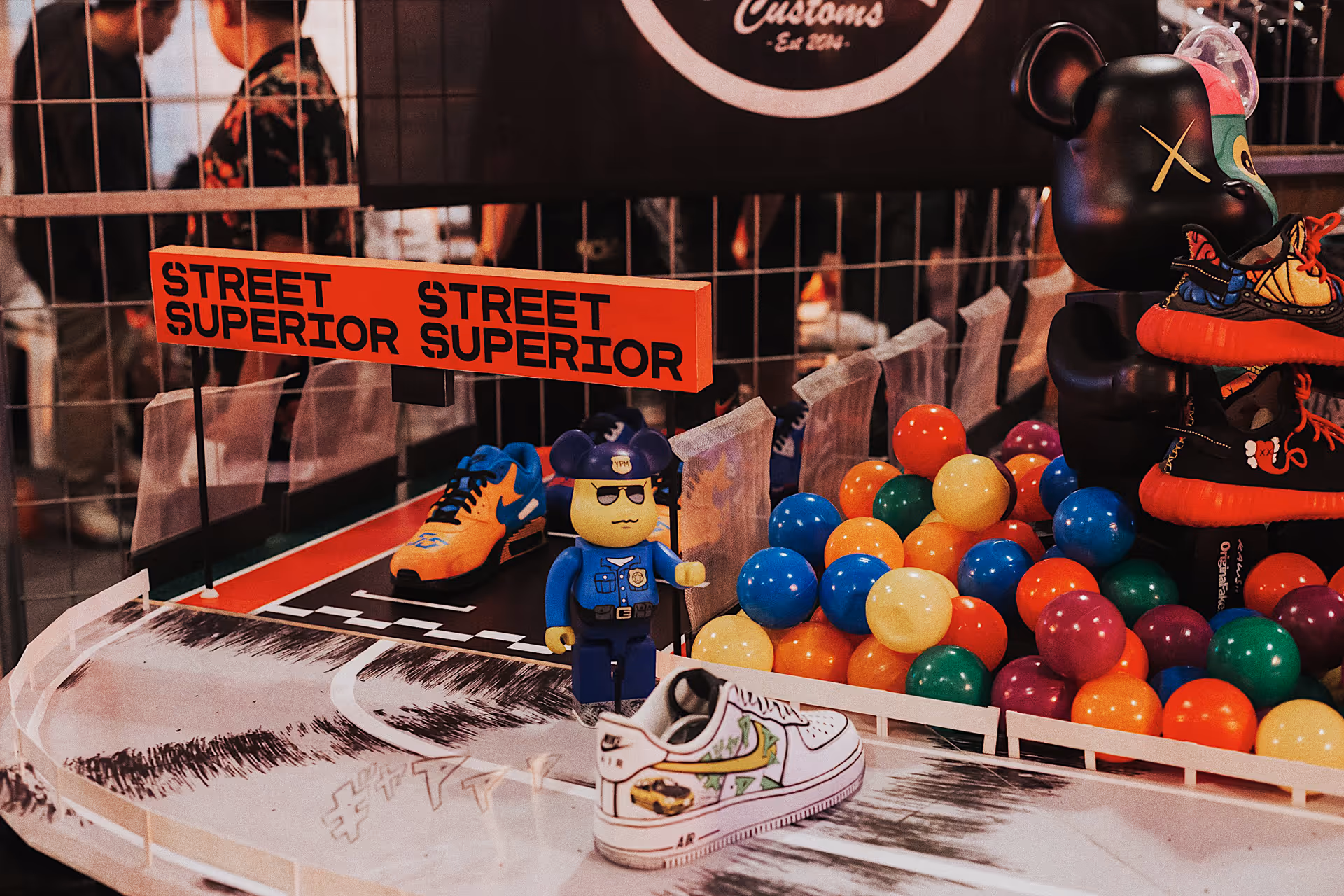 Display of colorful sneakers and toy figures, including a LEGO-like police officer and a black bear holding shoes, with a sign reading 'Street Superior.'