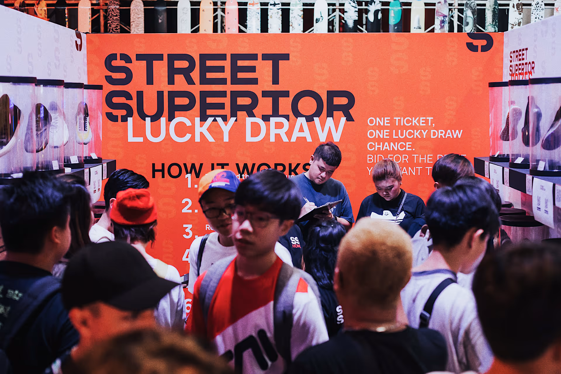 Crowd of people participating in the Street Superior Lucky Draw event in front of an orange informational wall with instructions.
