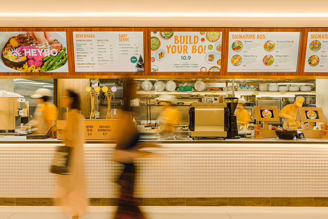 Blurred staff and customers moving in a modern fast-casual restaurant with menu boards displaying food and beverage options above the counter.