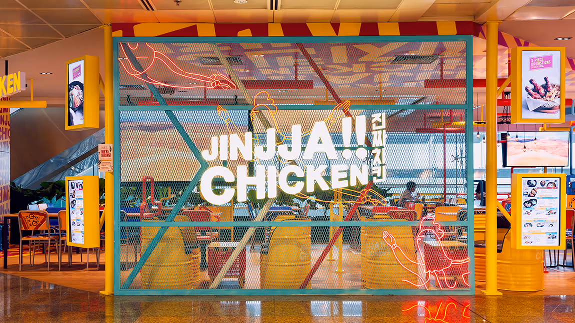 Entrance of JINJJA Chicken restaurant with yellow chairs, neon chicken illustrations, and menu displays.