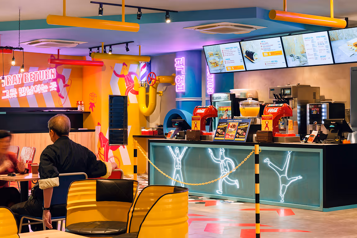Colorful restaurant interior with neon signage, cartoon wall art, and digital menu screens above the counter.