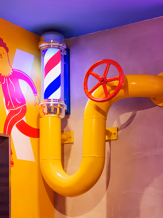 Yellow industrial pipe with a red valve wheel mounted on a wall next to an illuminated barber pole light fixture.