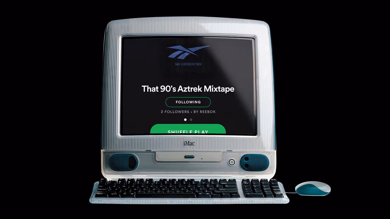 Vintage iMac computer displaying a Spotify playlist titled 'That 90's Aztrek Mixtape' with a Reebok logo and shuffle play button.