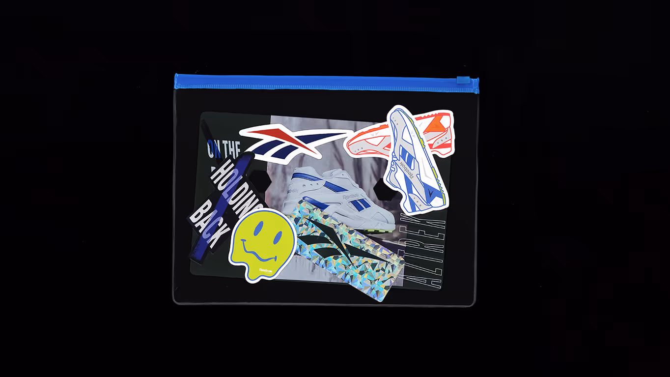 Black pouch with blue zipper featuring colorful Reebok-themed stickers including shoes, logo, smiley face, and text.