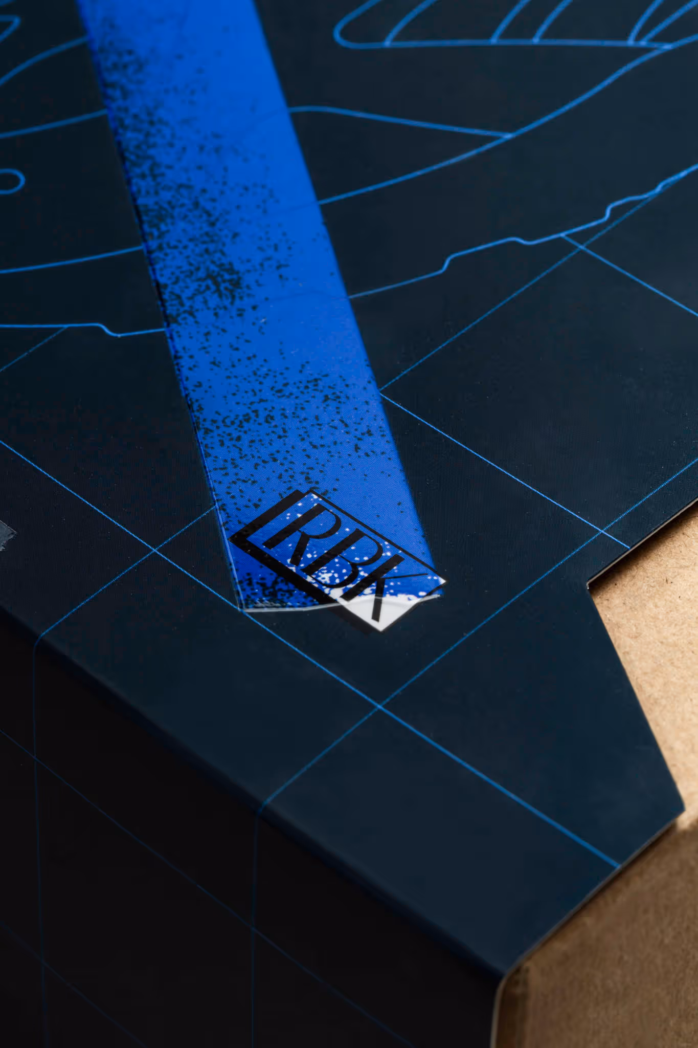 Close-up of a black and blue geometric patterned surface with the letters 'RBK' printed in a black box on a blue stripe.