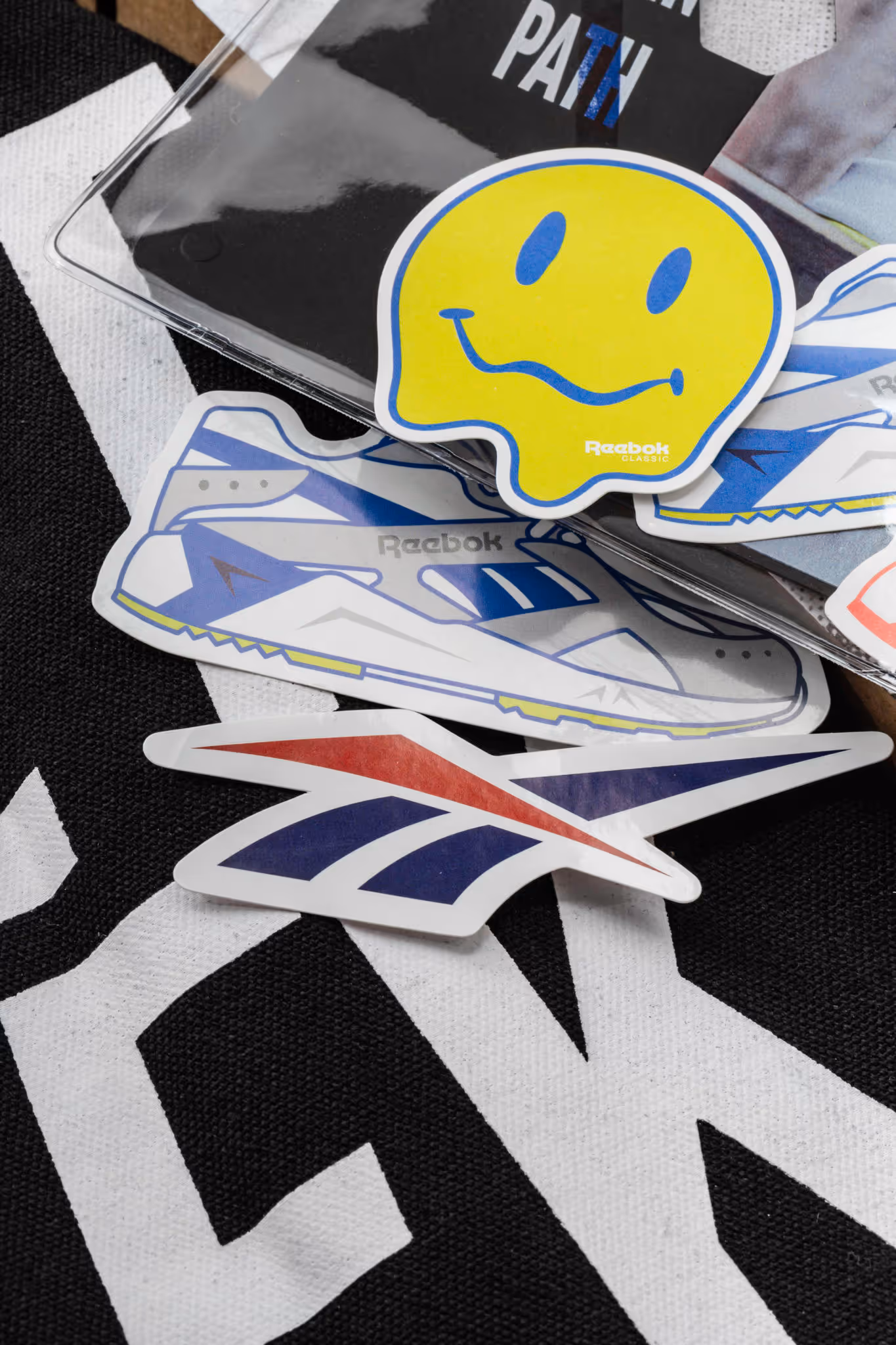 Collection of Reebok stickers including a yellow smiley face, a sneaker, and the Reebok logo on a black and white background.