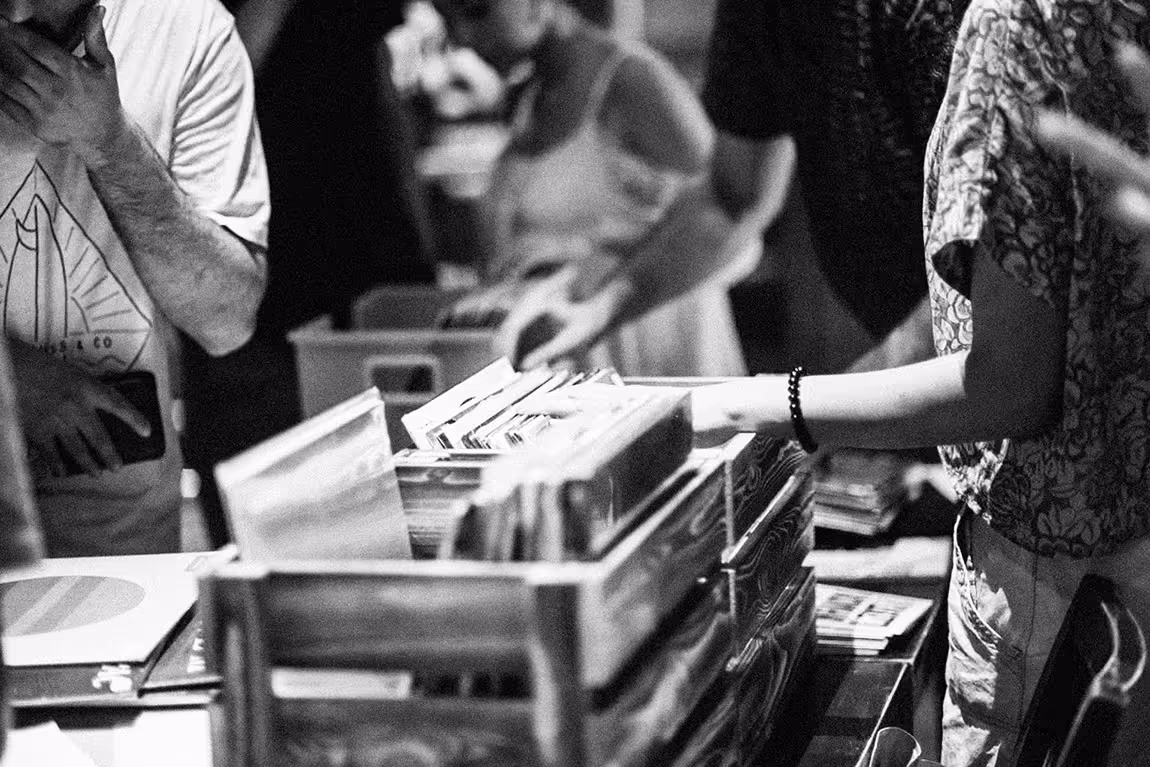 Black and white image of people flipping through vinyl records stored in wooden crates.