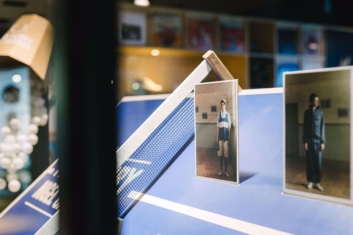Ping pong table with two photographs of people taped to the side, one wearing a sports outfit and the other in casual clothes.