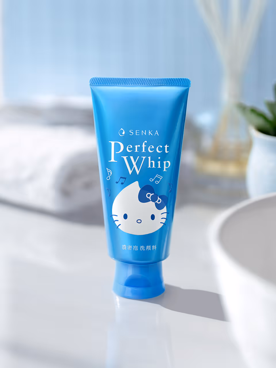 Blue tube of Senka Perfect Whip facial cleanser featuring a Hello Kitty graphic with musical notes on a white bathroom countertop.
