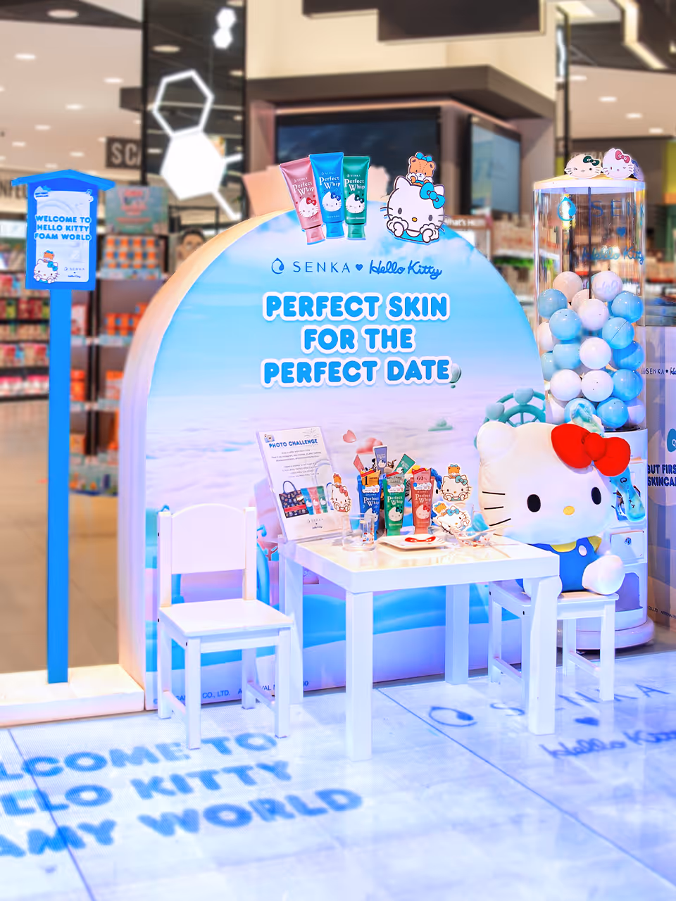 Hello Kitty-themed skincare display with products, a table and chairs, and a large Hello Kitty plush in a store setting.