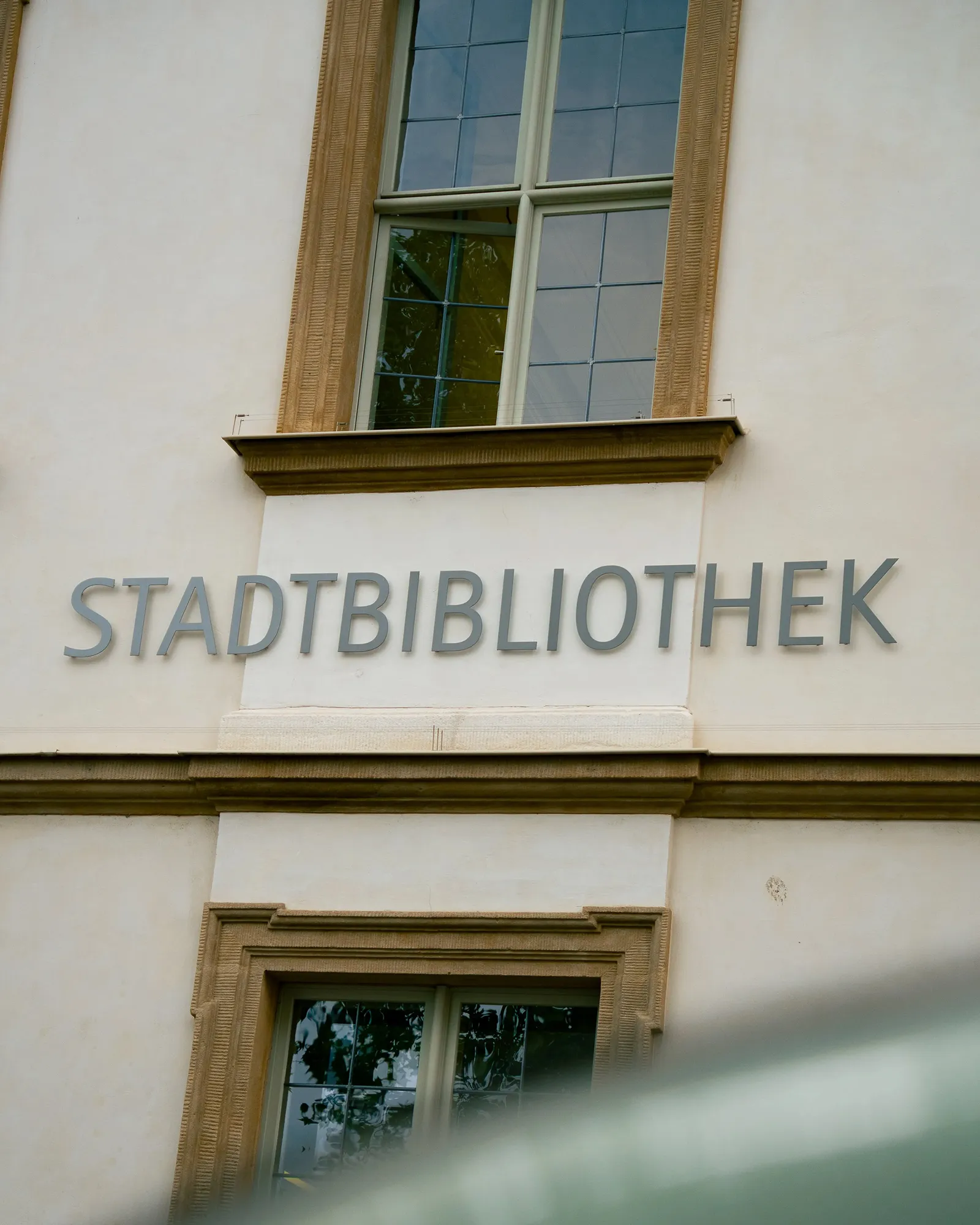 Exterior wall of a building with large windows and the word 'STADTBIBLIOTHEK' mounted on it.