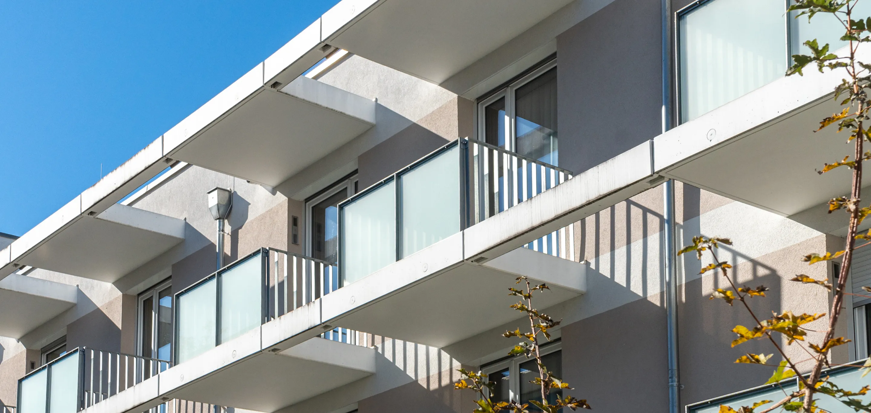 Modern apartment building balconies with frosted glass railings and metal bars against a clear blue sky.