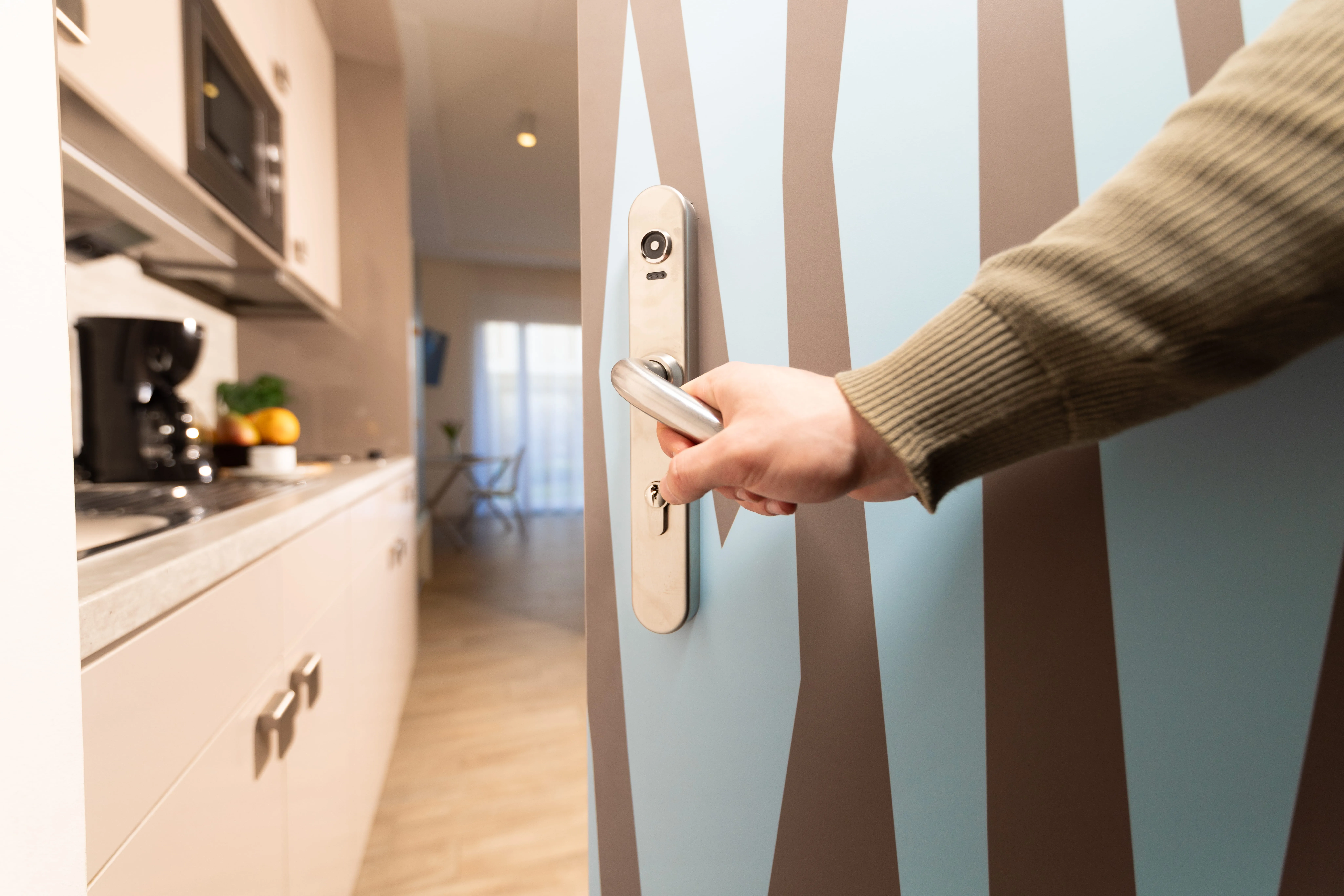 Person opening a door painted with brown tree trunks on a light blue background, leading into a modern kitchen.
