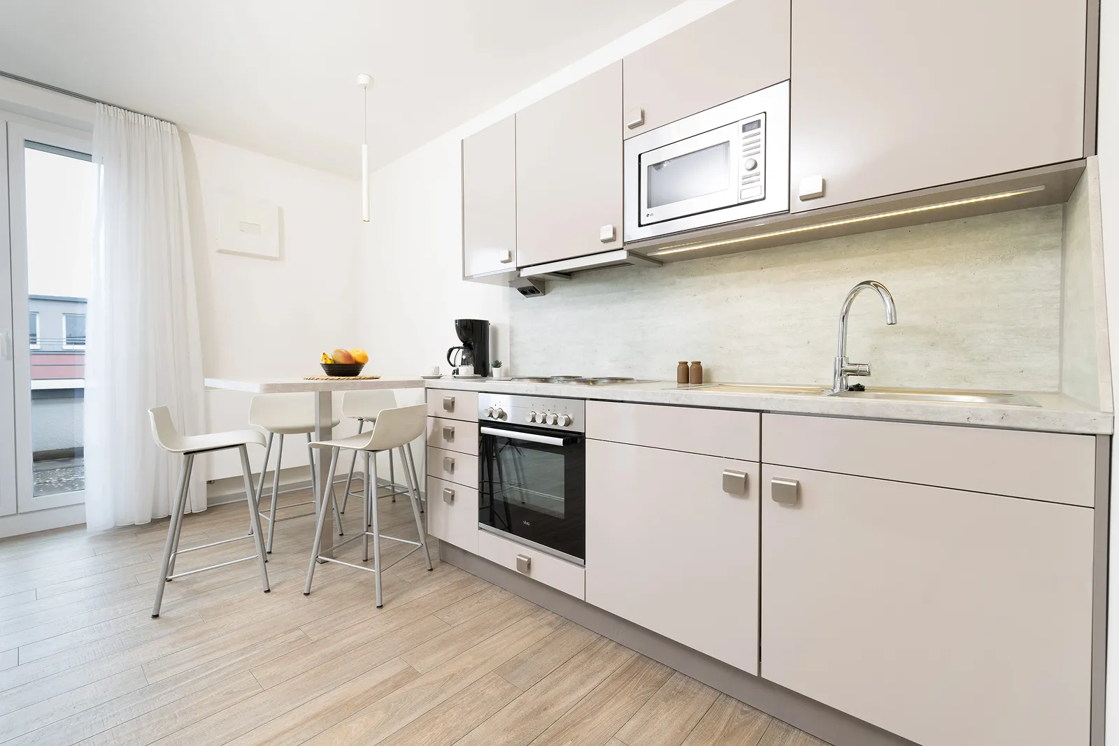 Modern hotel room with a large double bed, white bedding, patterned headboard and cabinets, wood-flooring, and a wall-mounted TV.