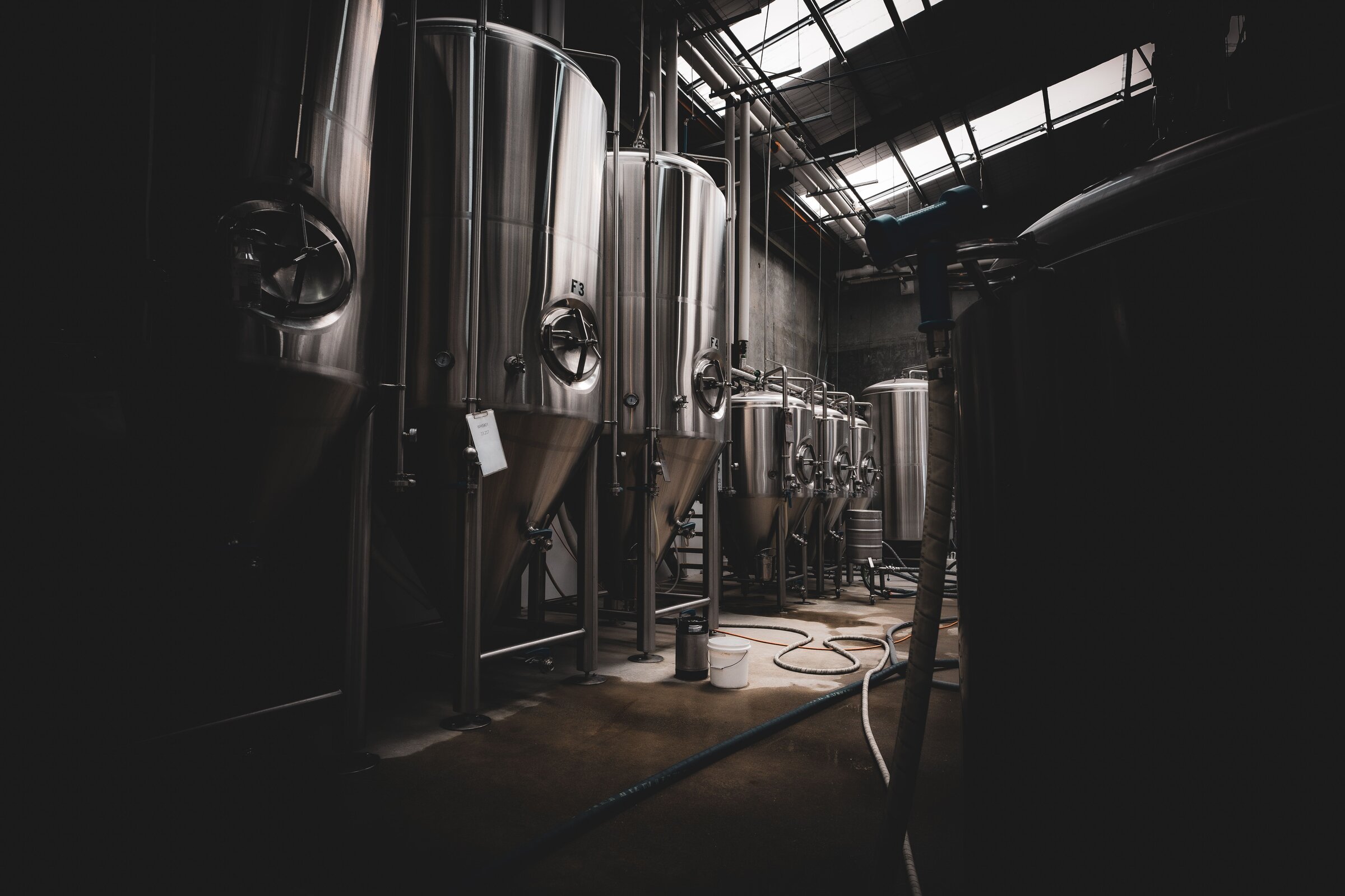Stainless steel fermentation tanks inside a dimly lit brewery
