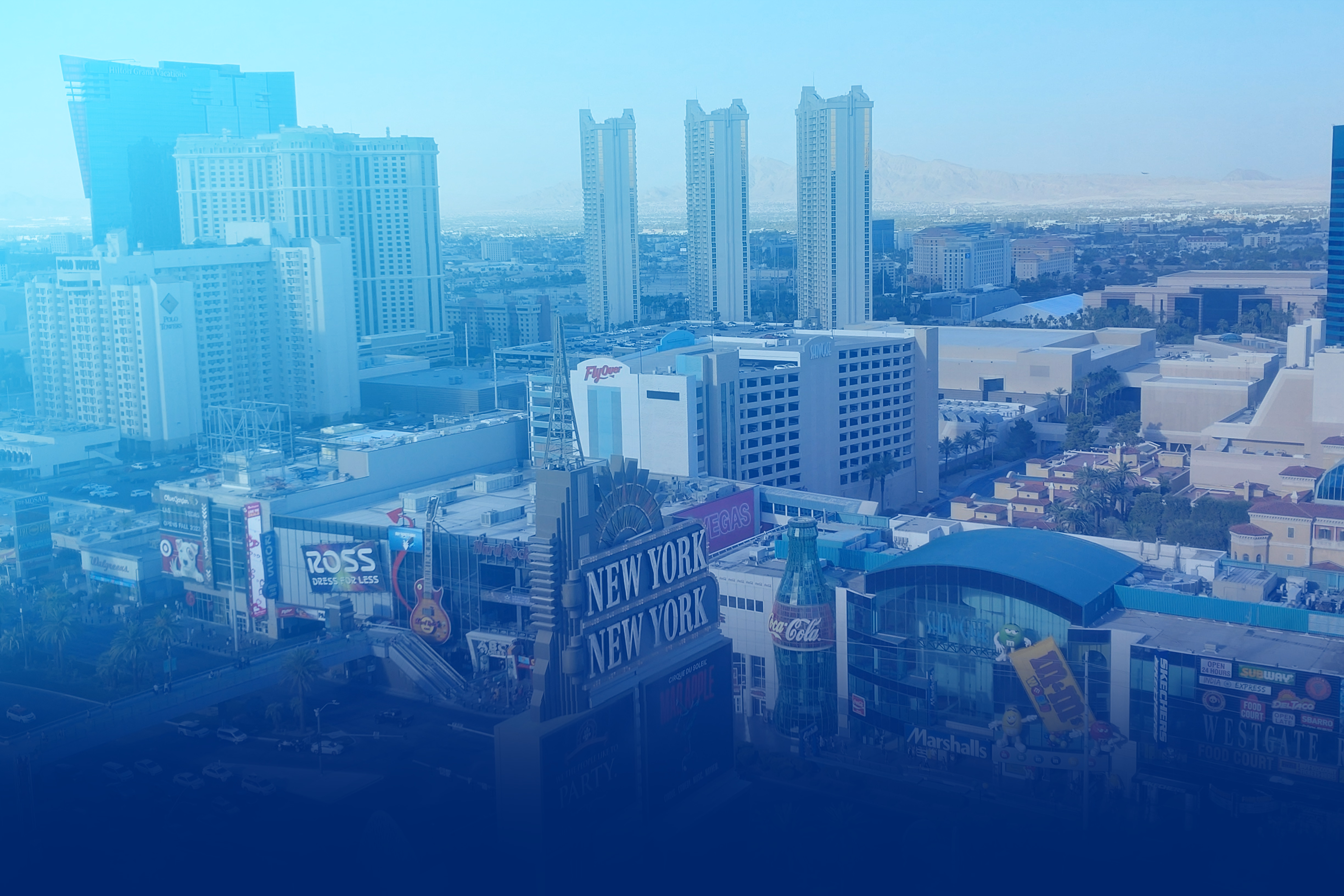 Aerial view of Las Vegas featuring the New York-New York hotel sign, a large Coca-Cola bottle, and surrounding city buildings under a clear sky.
