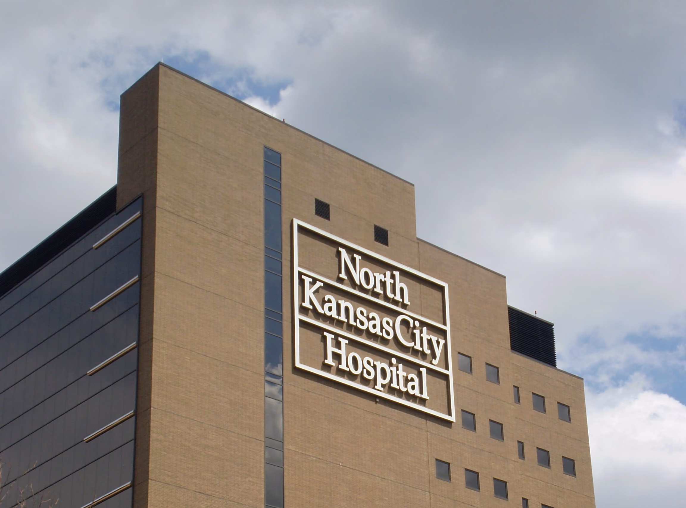 Tall North Kansas City Hospital building with brown exterior and numerous windows under a cloudy sky.