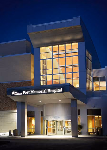 Night view of Fort Memorial Hospital entrance with illuminated glass windows and signage.