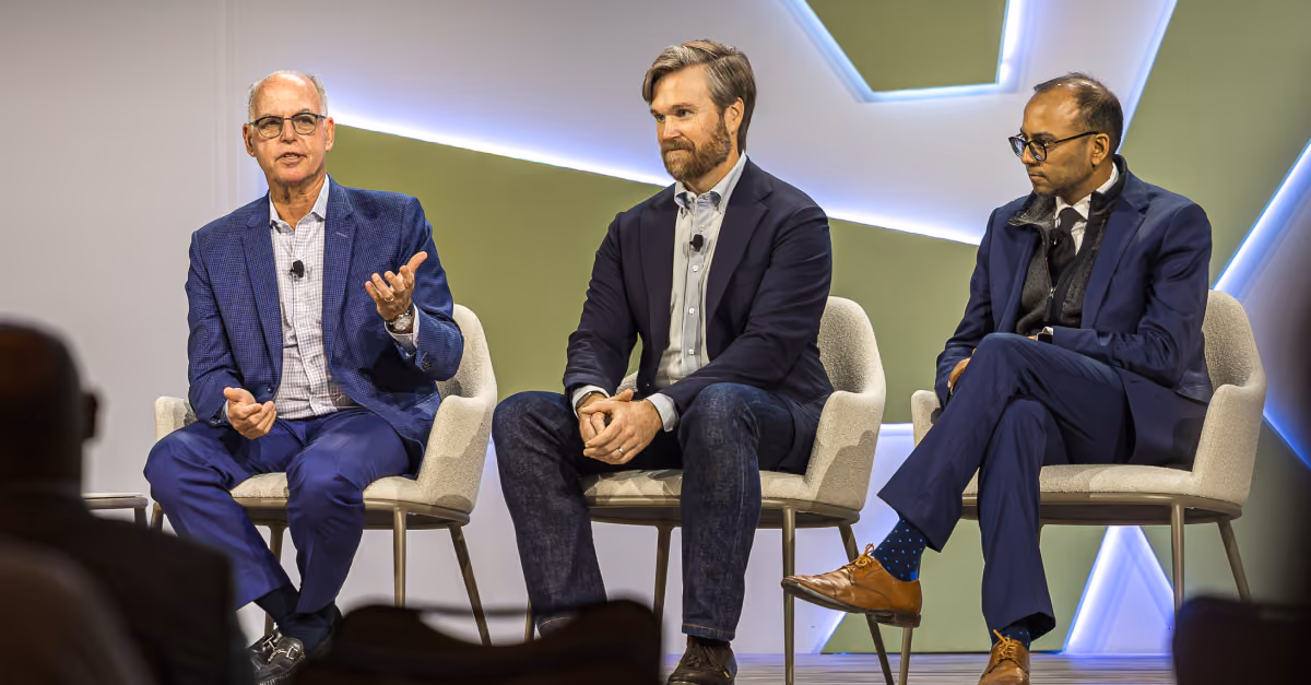 Three men seated on stage chairs during a panel discussion at a conference.