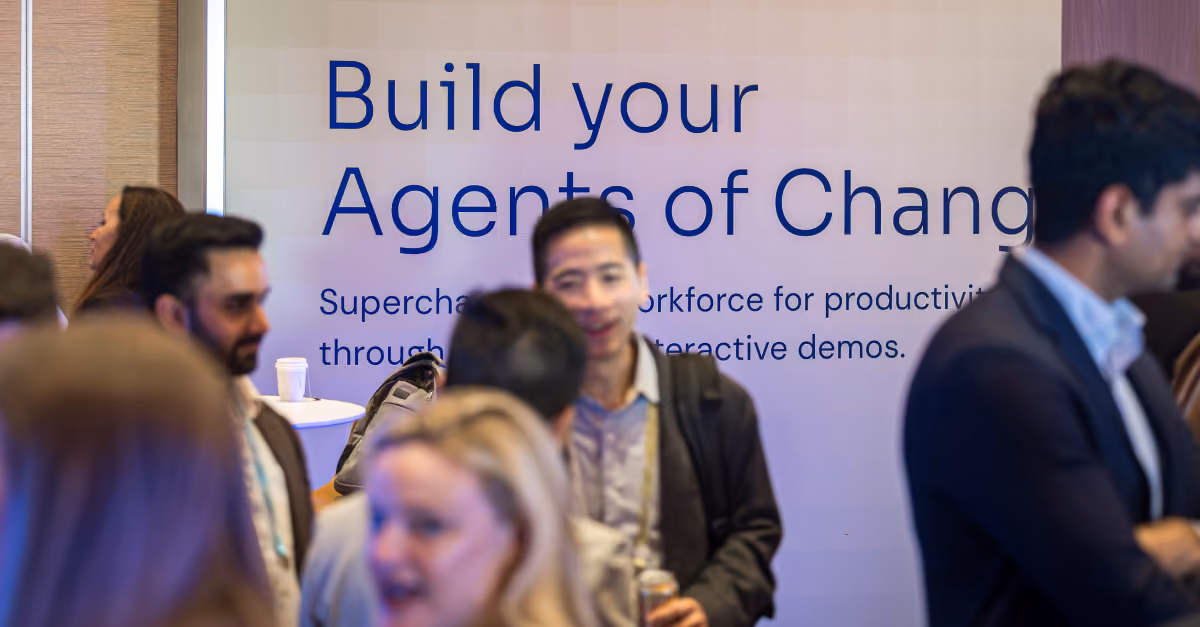 People talking in front of a banner reading 'Build your Agents of Change' at an event.