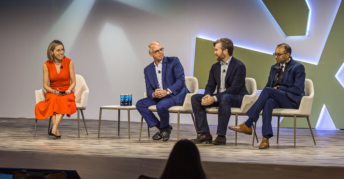 Four panelists seated on stage in a discussion, with a woman in red and three men in suits.