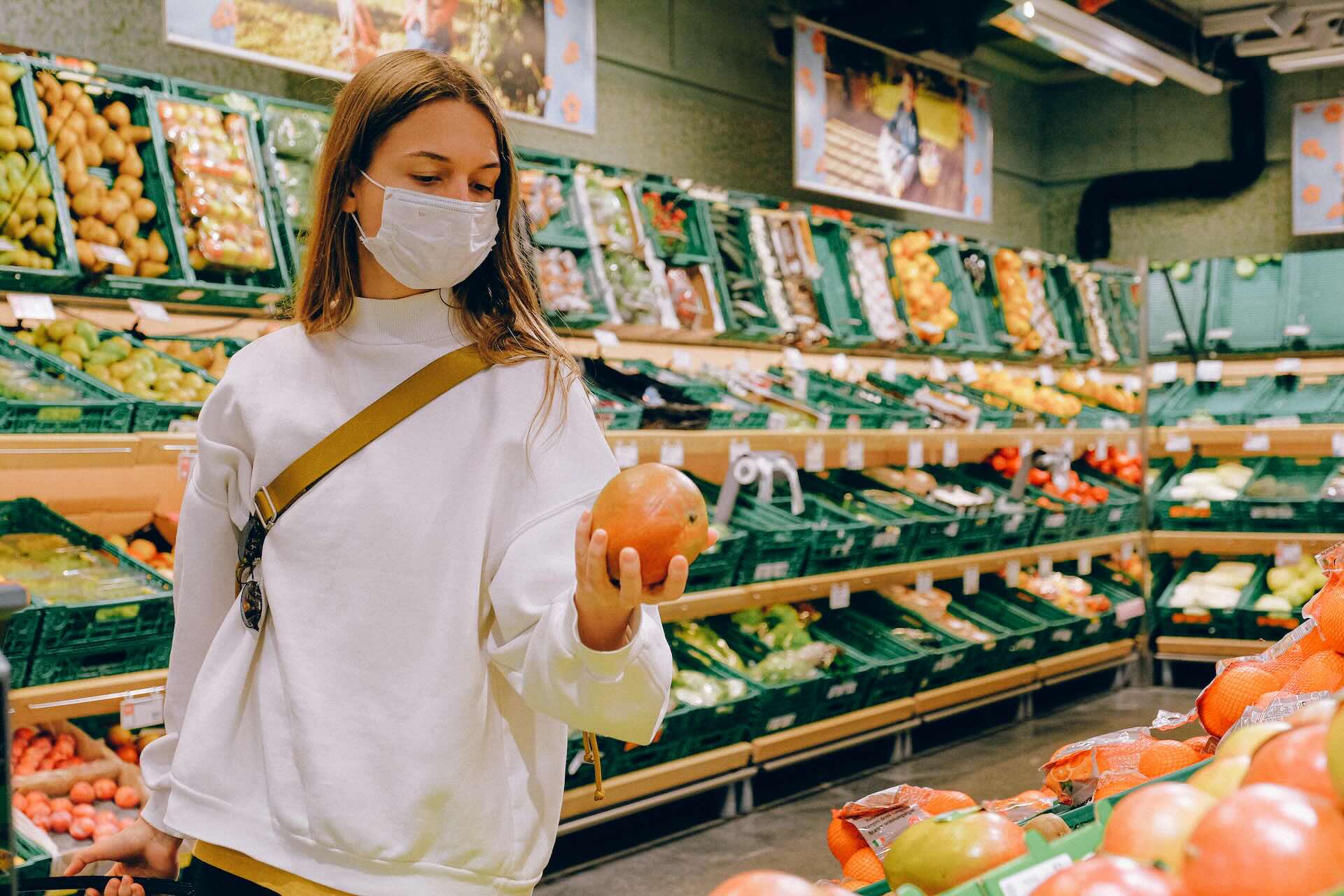 Woman wearing a mask inspects a mango in a grocery store