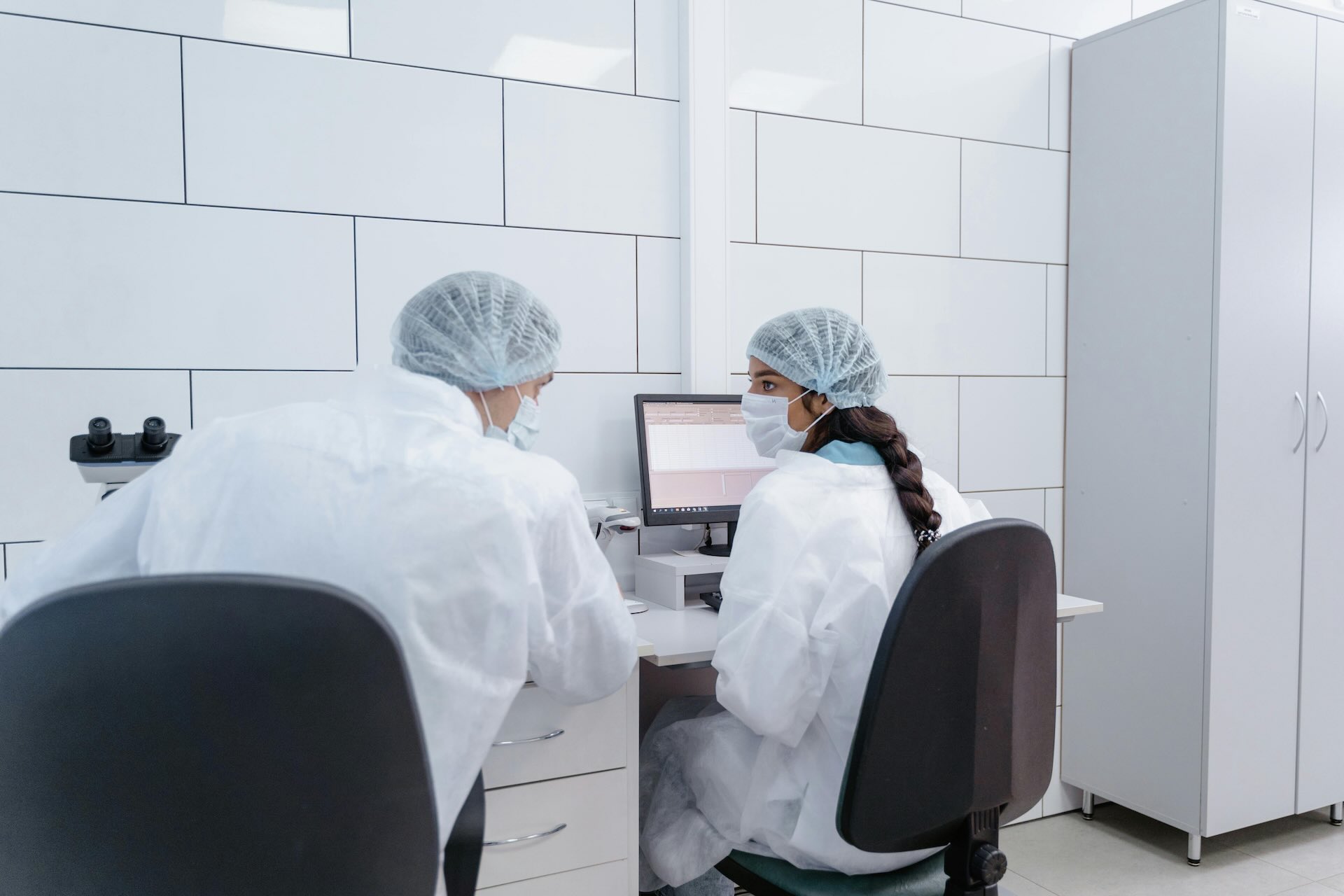 Two food safety lab technicians in protective gear reviewing data on a computer