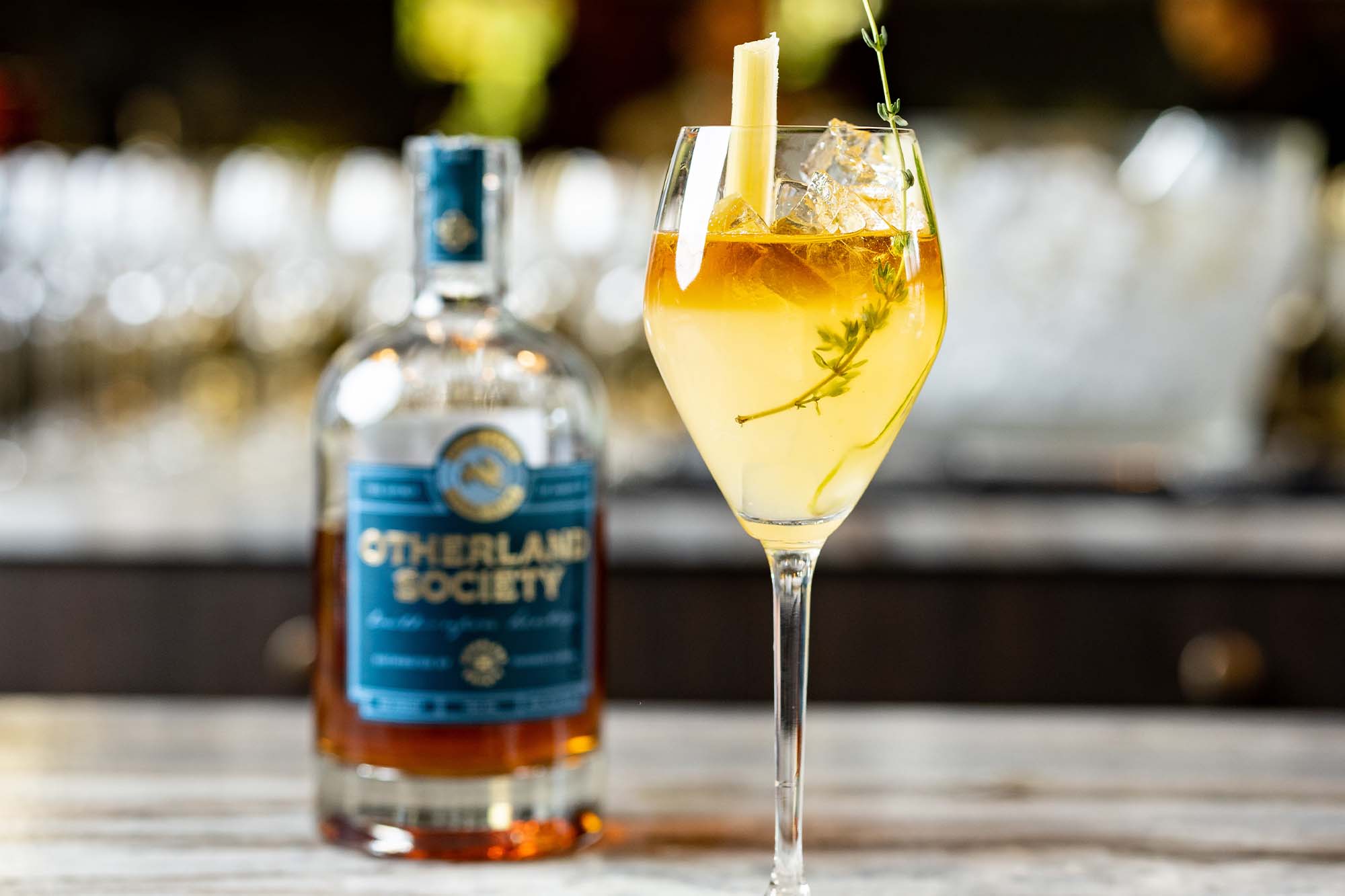 Hurricane Thyme drink in a cocktail glass in front of bottle of Otherland Society Wild Hare Dark Rum